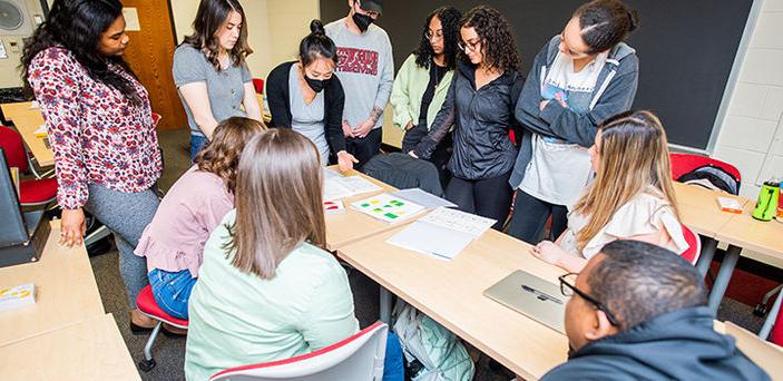 Professor Alice Cheng leaning over a classroom table showing materials to students who are gathered around the table